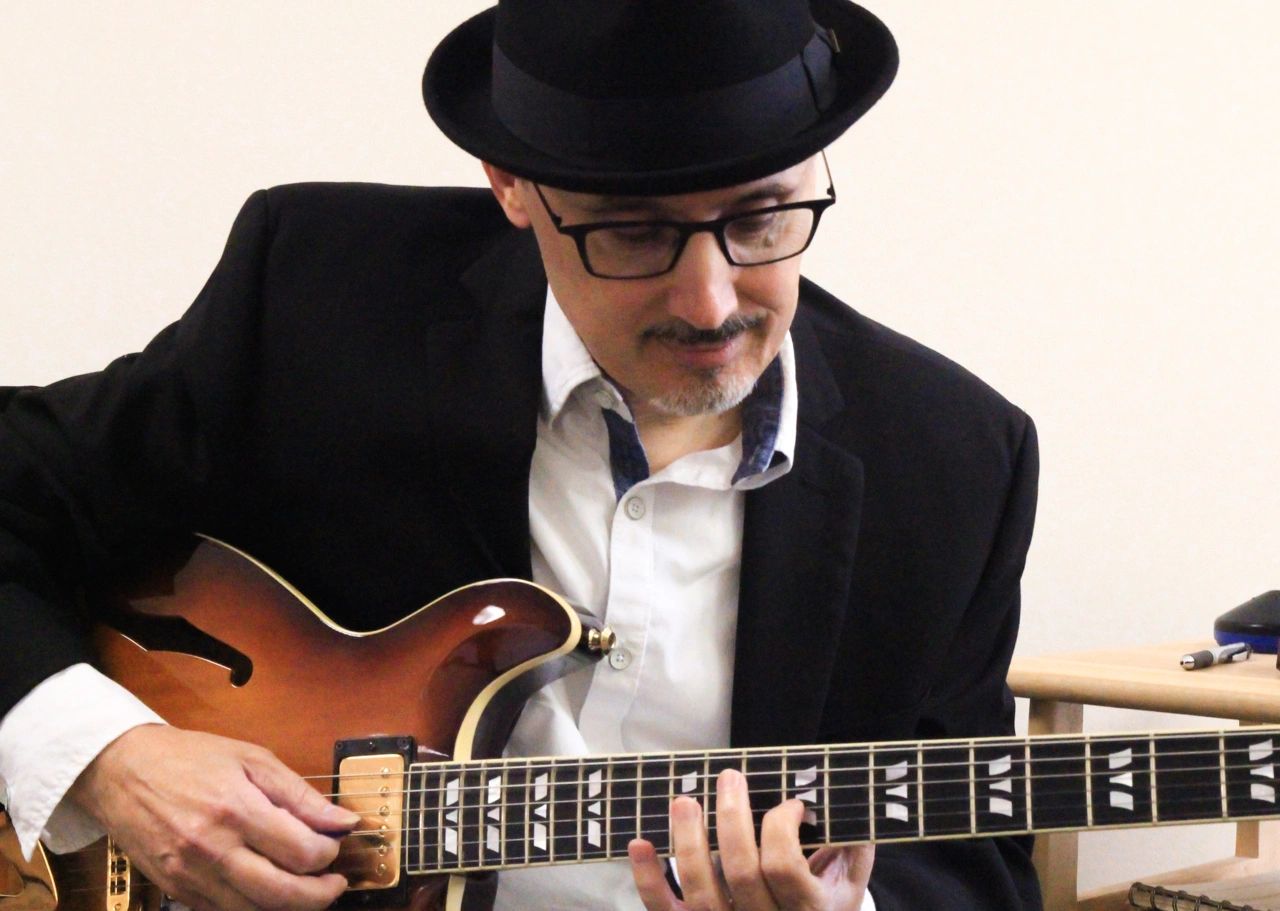 A man in a hat and glasses playing an electric guitar.