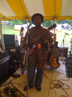 A man in a brown shirt and hat playing guitar.