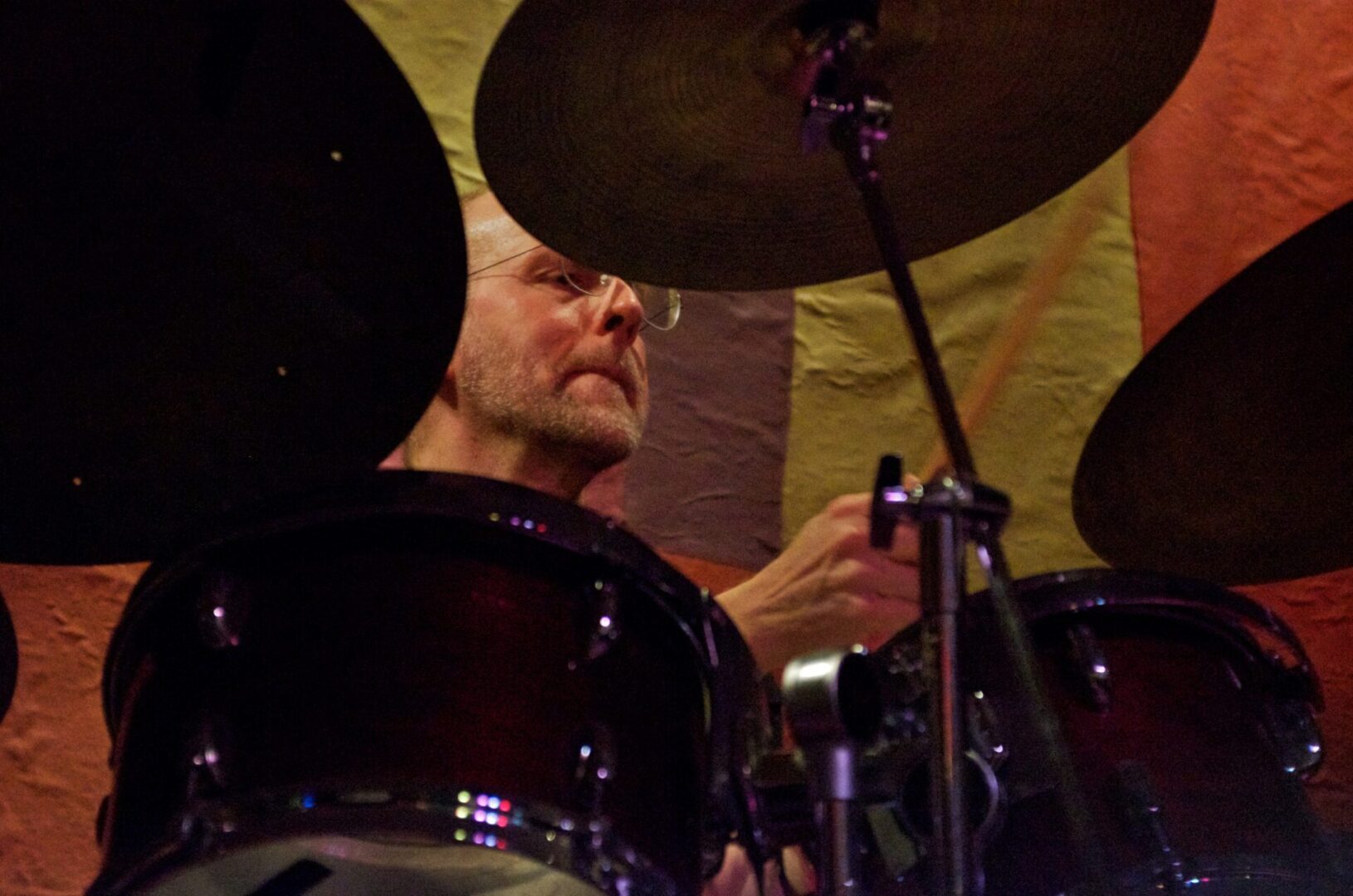 A man playing drums in front of a yellow wall.