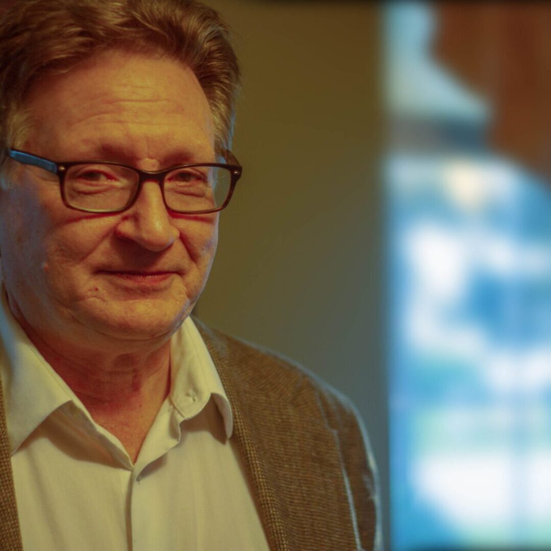 A man with glasses is standing in front of a window.