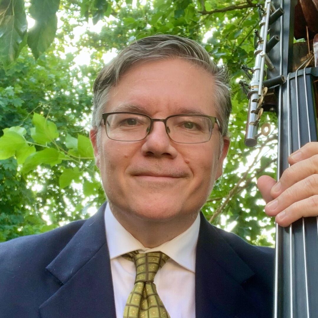 A man in suit and tie holding a bass.