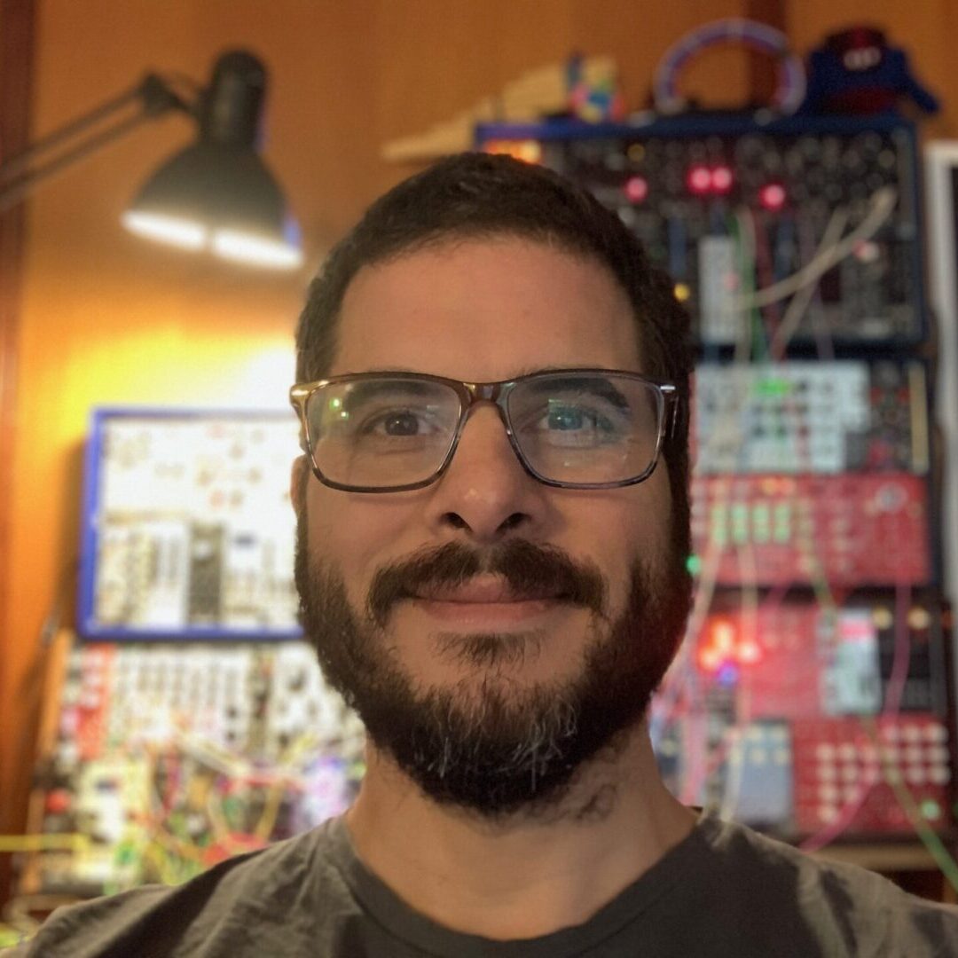 A man with glasses and beard in front of a wall.